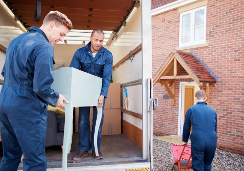 Removal Company Workers Unloading Furniture And Boxes From Truck Into New Home On Moving Day